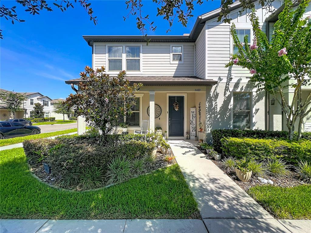 A two-story suburban house features light-colored siding, a covered front porch, and a landscaped yard — 5069 CASPIAN STREET, ST CLOUD, FL