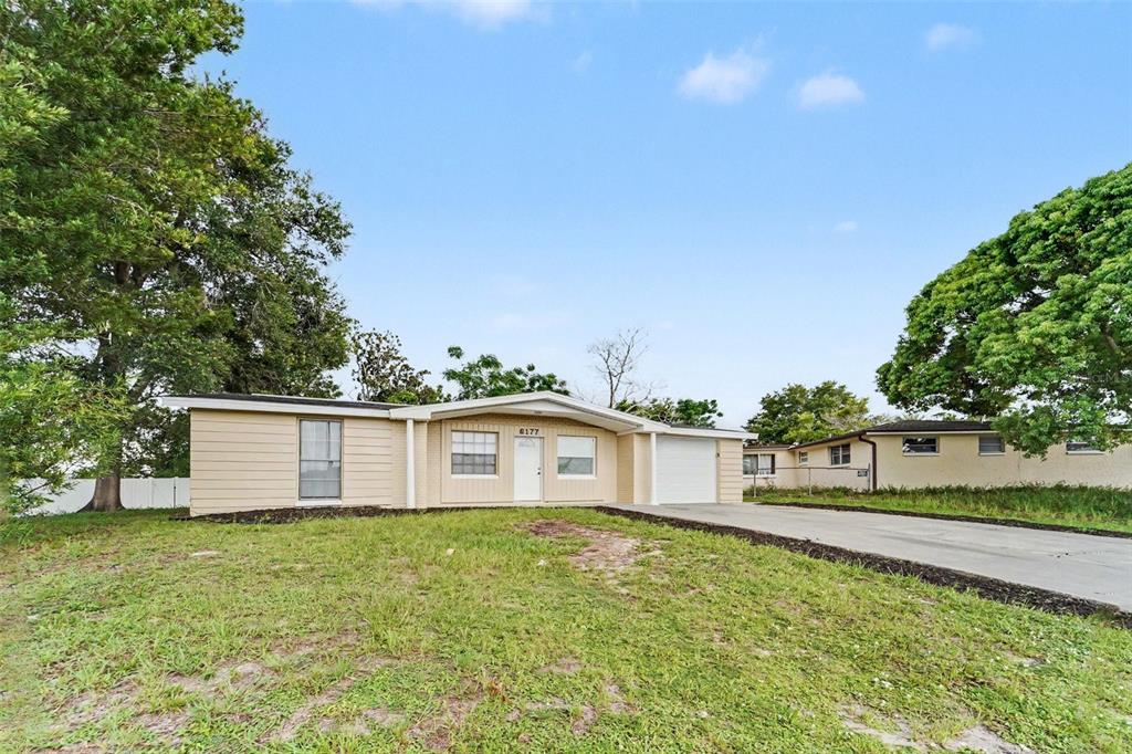 A single-story house with beige siding, a white garage door, and a concrete driveway — 6177 MAPLEWOOD DRIVE, NEW PORT RICHEY, FL