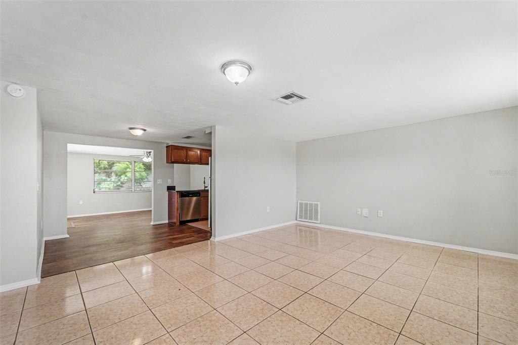 A living room with light-colored tile flooring transitions into a kitchen with dark wood cabinets — 6177 MAPLEWOOD DRIVE, NEW PORT RICHEY, FL