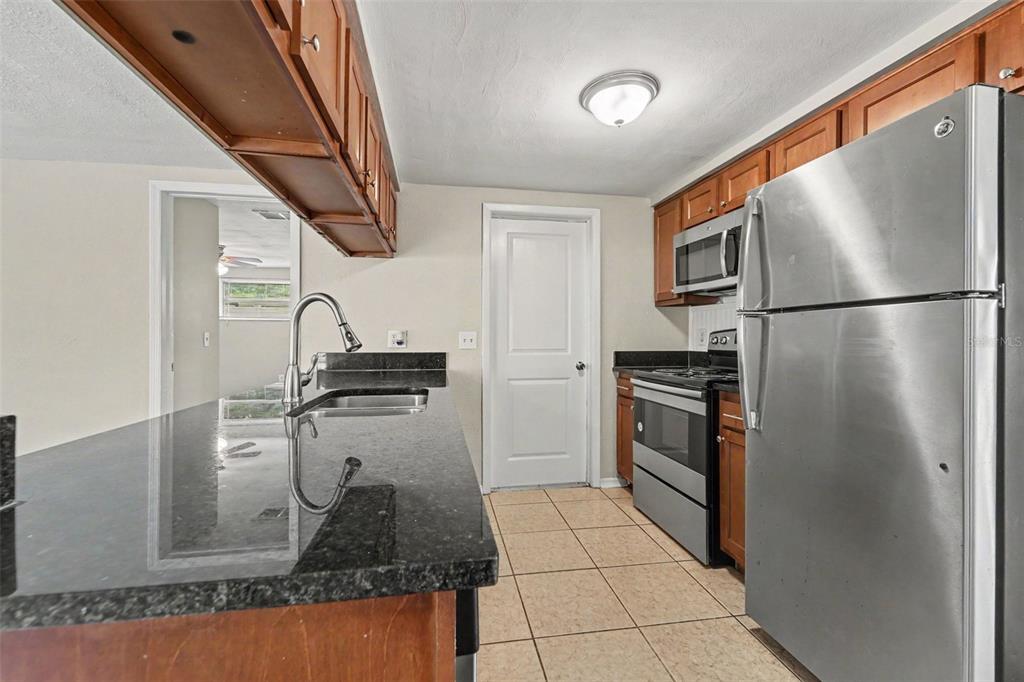 A kitchen features dark granite countertops, wood cabinetry, stainless steel appliances, and tile flooring — 6177 MAPLEWOOD DRIVE, NEW PORT RICHEY, FL