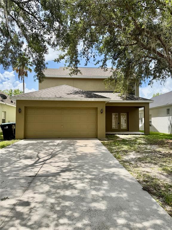 A two-story tan house features a two-car garage, a covered entryway, and mature trees — 14205 BRIDGEWATER CROSSINGS BOULEVARD, WINDERMERE, FL