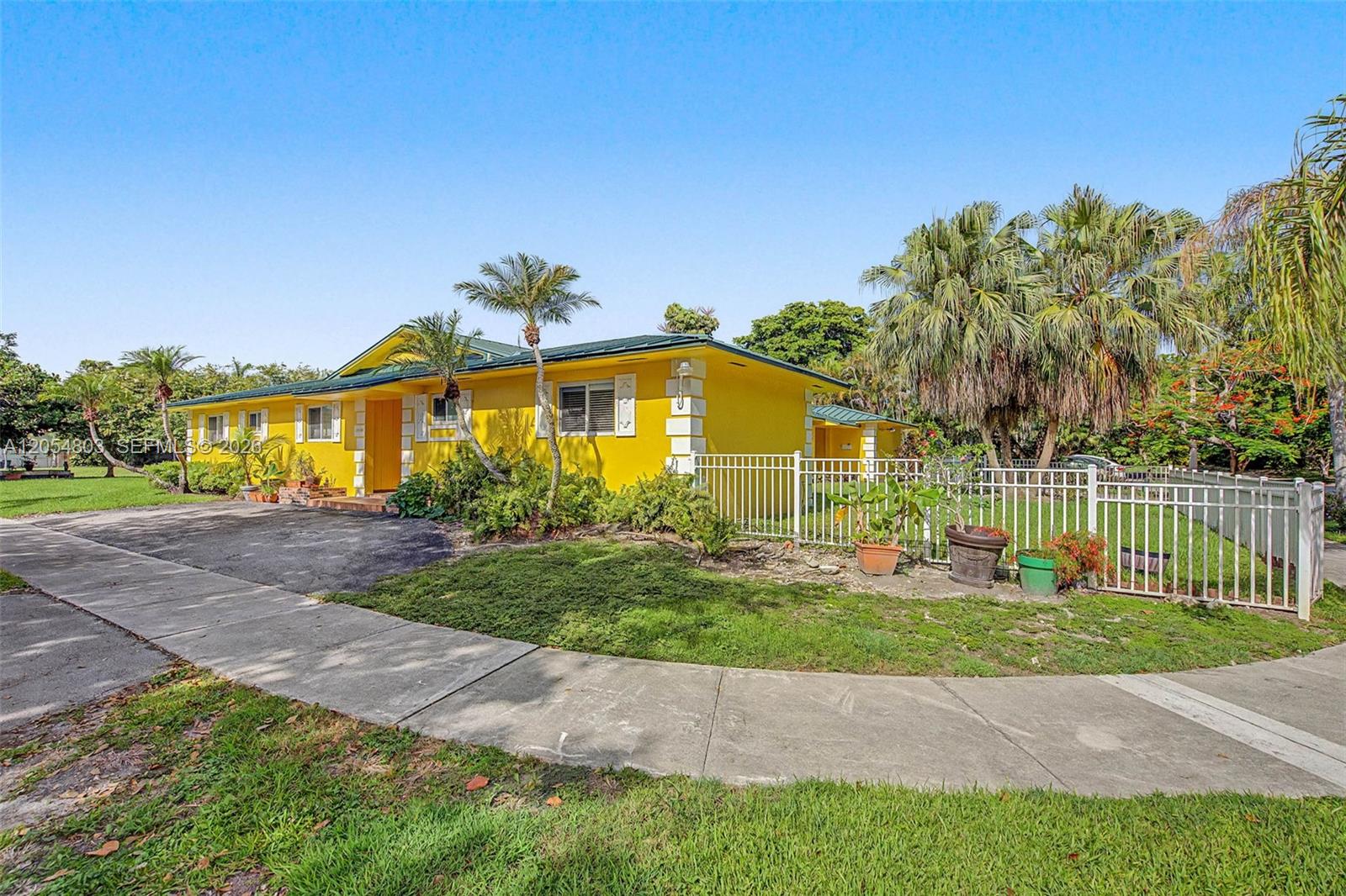 A bright yellow single-story house features a green roof, white trim, and a fenced yard — 10650 SW 77th Ct, Pinecrest FL 33156, PINECREST, FL