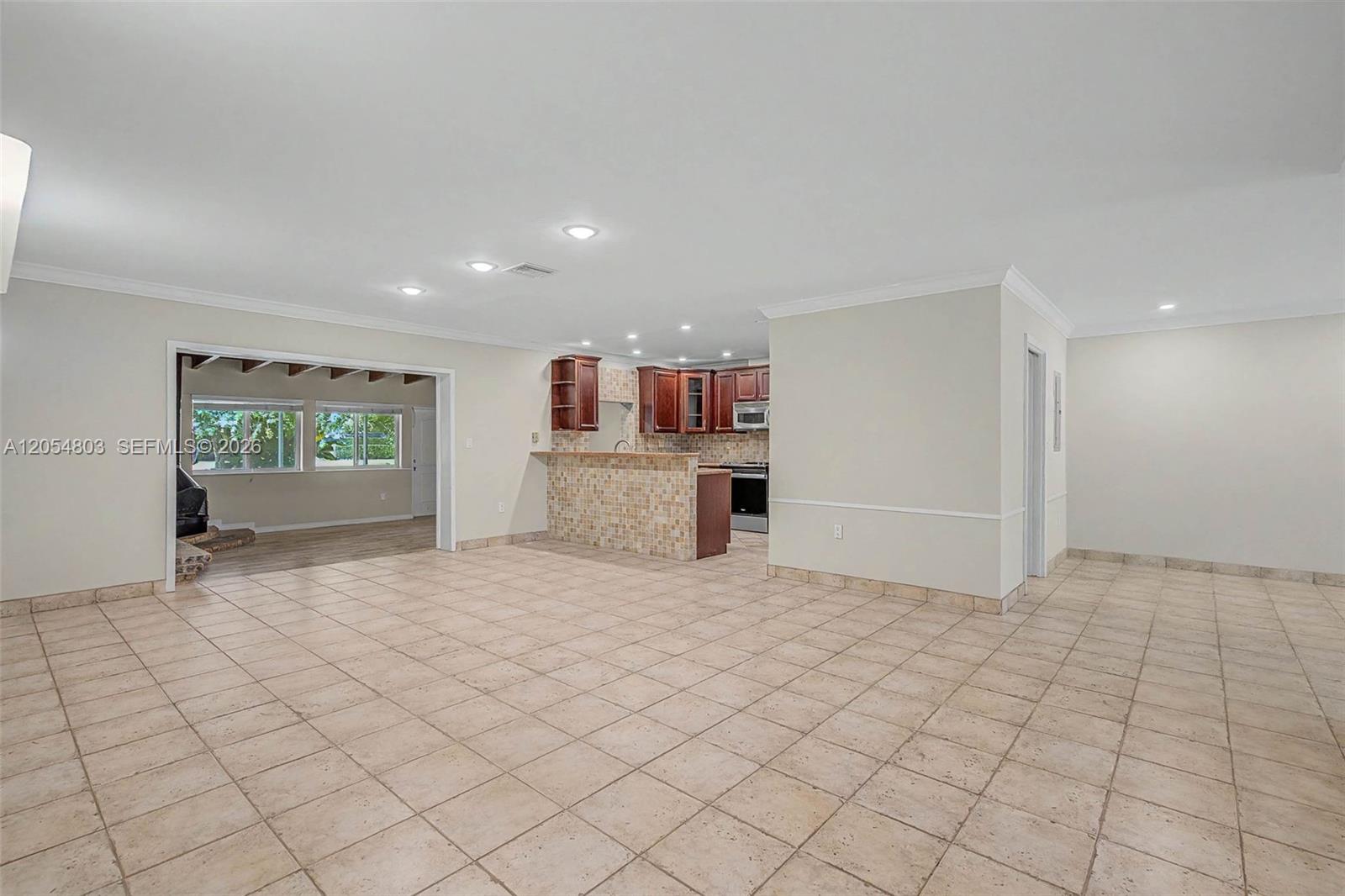 An open-concept living area features tiled floors, a kitchen with wood cabinets, and a breakfast bar — 10650 SW 77th Ct, Pinecrest FL 33156, PINECREST, FL