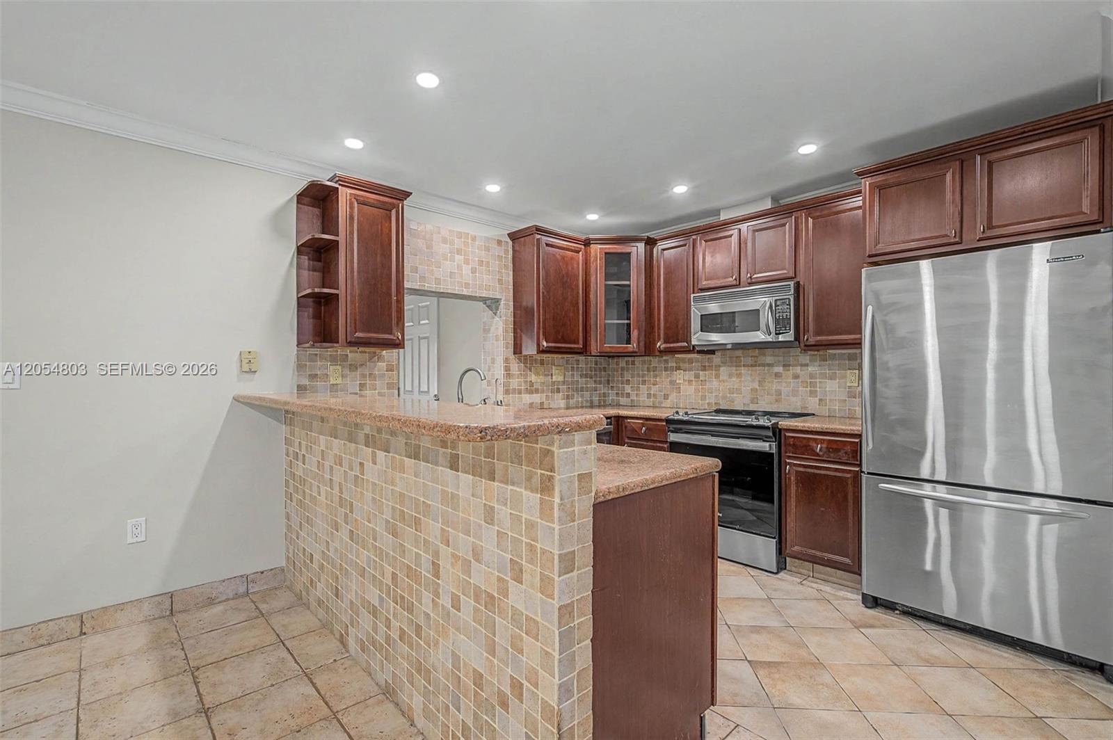 A kitchen features dark wood cabinets, granite countertops, tiled backsplashes, and stainless steel appliances — 10650 SW 77th Ct, Pinecrest FL 33156, PINECREST, FL