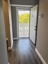 A hallway with wood-look flooring leads to an open door with a security screen — 1025 SE 3rd Avenue # 303, Dania Beach FL 33004, DANIA BEACH, FL