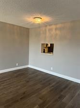 An empty room with dark wood-look flooring, light gray walls, and a kitchen pass-through window — 1025 SE 3rd Avenue # 303, Dania Beach FL 33004, DANIA BEACH, FL