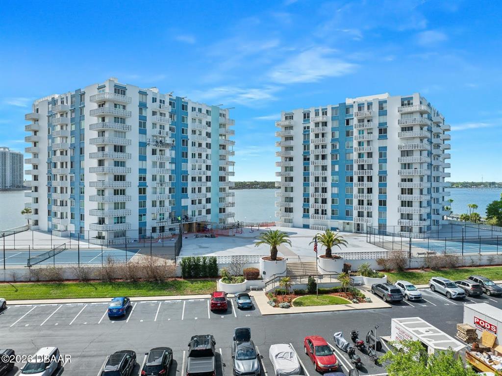 An exterior view shows two tall residential buildings situated along a waterfront with a parking lot — 925 N HALIFAX AVENUE UNIT 204, DAYTONA BEACH, FL