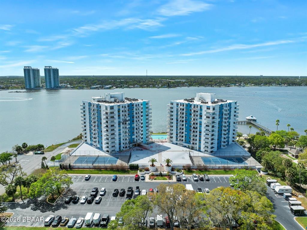 An aerial view shows two high-rise apartment buildings situated along a waterfront with tennis courts — 925 N HALIFAX AVENUE UNIT 204, DAYTONA BEACH, FL