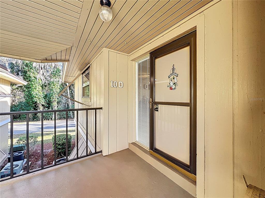 A covered balcony features a brown screen door, a light fixture, and a metal railing — 130 JASMINE WOODS COURT UNIT 10D, DELTONA, FL