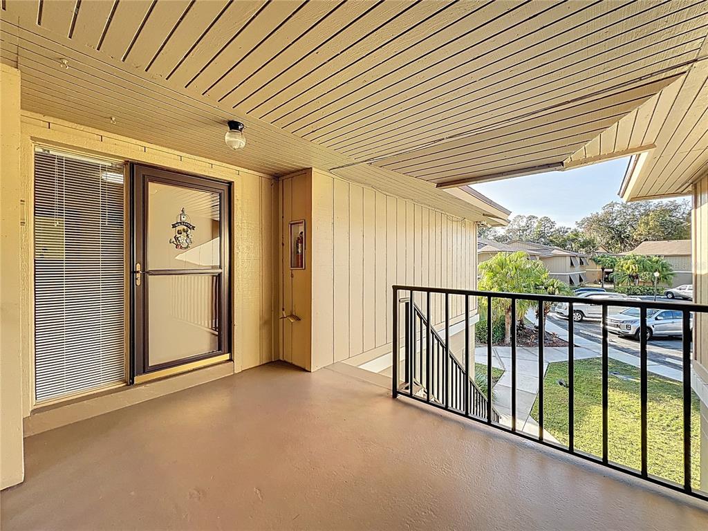 A covered balcony features a beige exterior, a metal railing, and a glass storm door — 130 JASMINE WOODS COURT UNIT 10D, DELTONA, FL