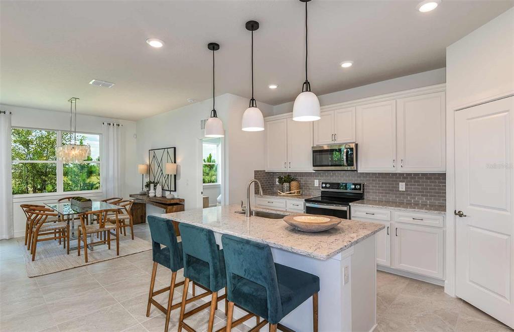 A kitchen with white cabinets, a granite island, and teal stools next to a dining area — 8581 SW 65TH STREET ROAD, OCALA, FL