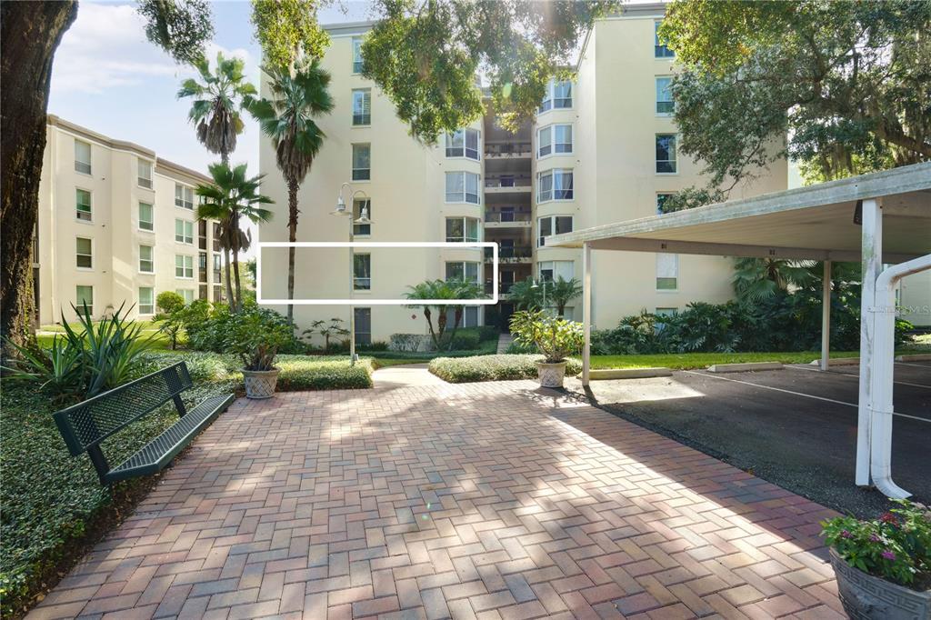 An exterior view of a multi-story apartment building with a paved courtyard and covered parking — 204 QUAYSIDE CIRCLE UNIT 201, MAITLAND, FL