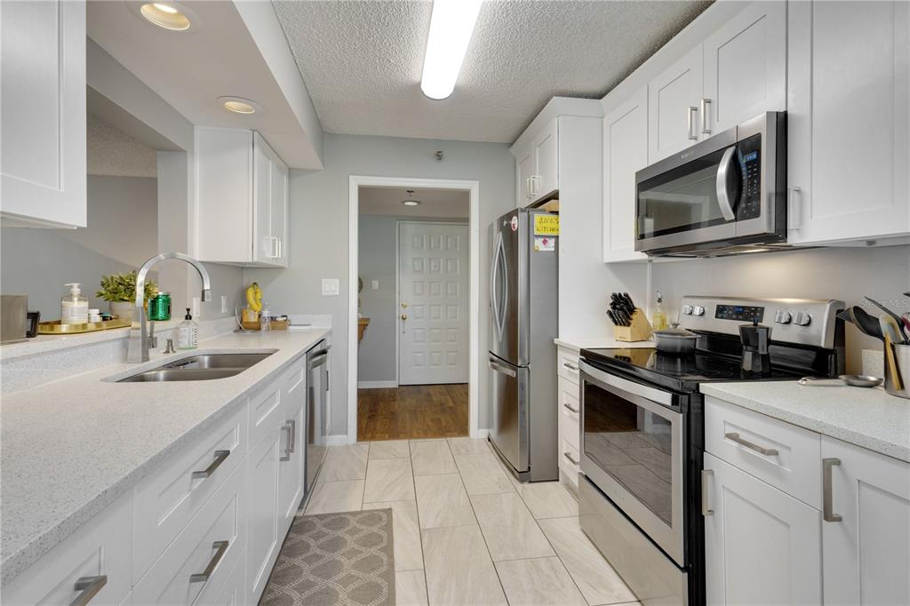 A galley kitchen features white cabinets, stainless steel appliances, and light-colored countertops — 204 QUAYSIDE CIRCLE UNIT 201, MAITLAND, FL