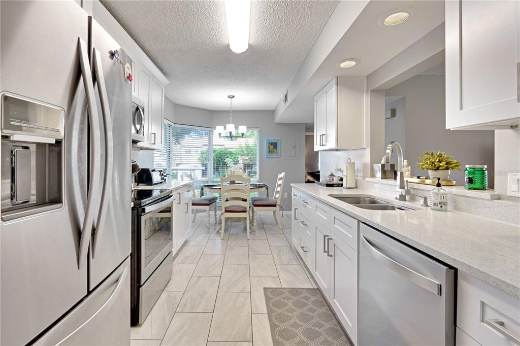 A kitchen features white cabinetry, stainless steel appliances, quartz countertops, and a dining area beyond — 204 QUAYSIDE CIRCLE UNIT 201, MAITLAND, FL