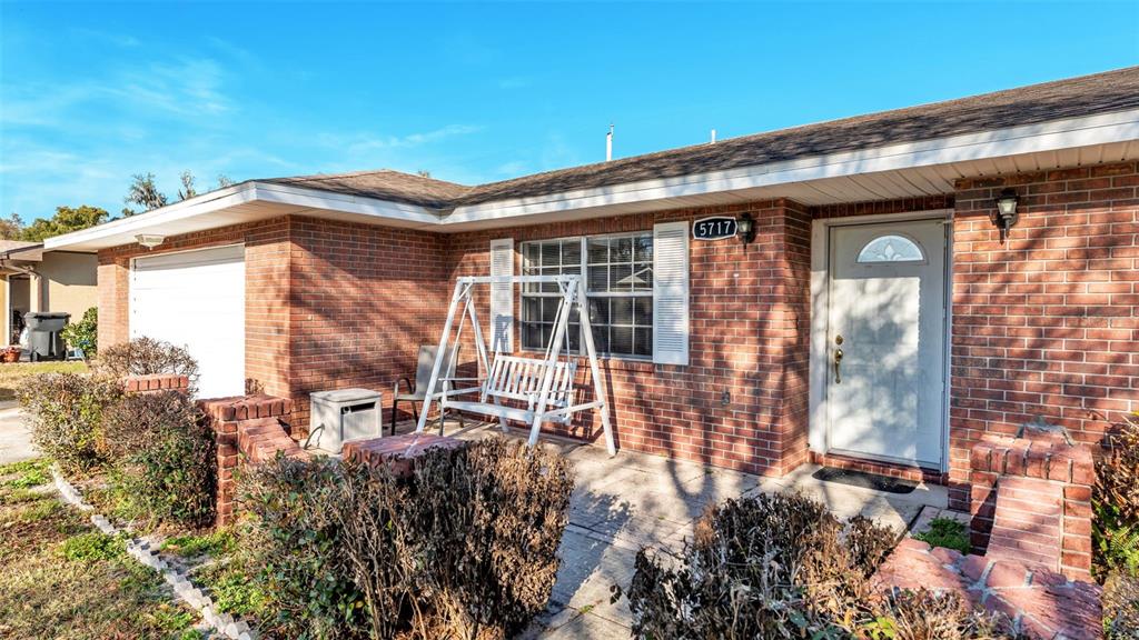 A brick house exterior features a white front door, a porch swing, and a garage — 5717 LAKE GROVE DRIVE, LAKELAND, FL