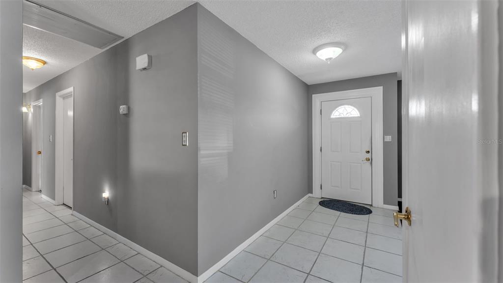 A tiled entryway features gray walls, a white front door, and a hallway with doors — 5717 LAKE GROVE DRIVE, LAKELAND, FL
