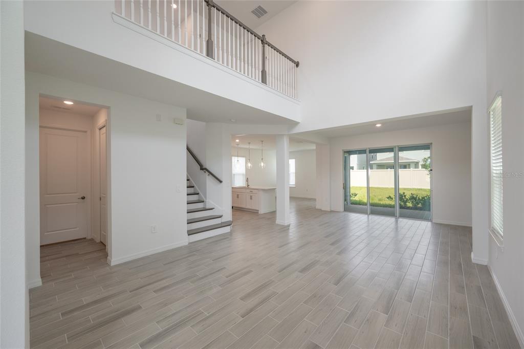A bright, open-concept living area features high ceilings, wood-look tile flooring, and a staircase — 1029 LADYFISH TRAIL, ST CLOUD, FL