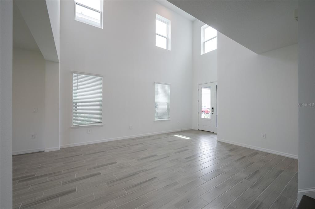 A bright, empty living room features high ceilings, white walls, and light gray wood-look flooring — 1029 LADYFISH TRAIL, ST CLOUD, FL