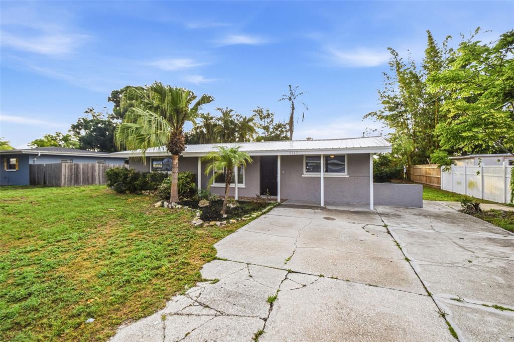 A single-story gray house features a metal roof, a front porch, and a cracked concrete driveway — 5917 OLIVE AVENUE, SARASOTA, FL