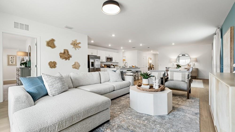 A bright, open-concept living room features a sectional sofa, white coffee table, and kitchen area — 5454 ISLA SAONA DRIVE, KISSIMMEE, FL