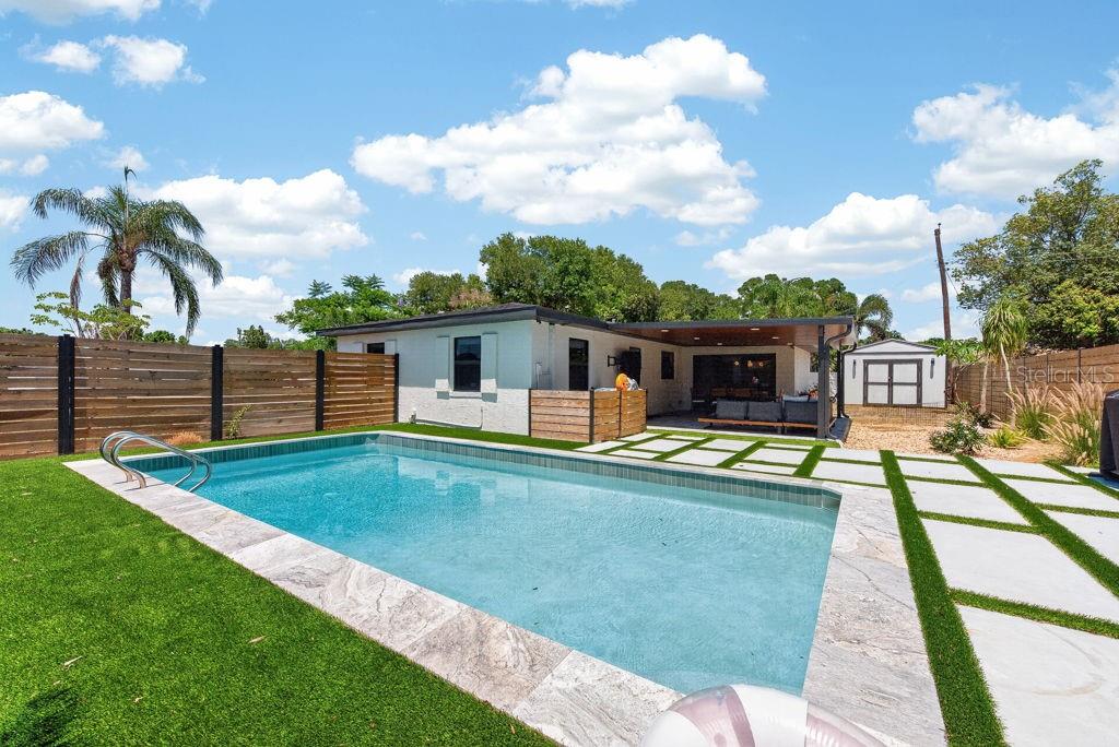 A backyard features a rectangular swimming pool, a covered patio, and a white storage shed — 6196 44TH AVENUE N, ST PETERSBURG, FL