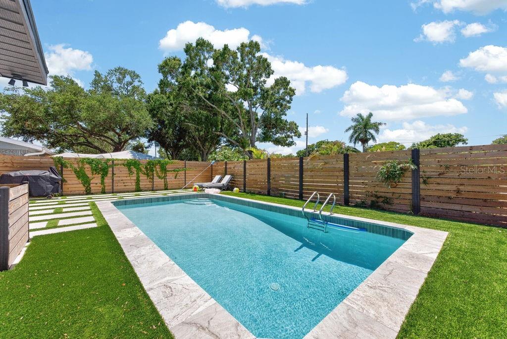 A rectangular swimming pool with a stone deck is surrounded by artificial turf and fencing — 6196 44TH AVENUE N, ST PETERSBURG, FL