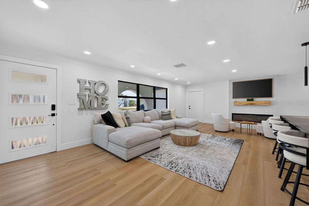 A modern living room features a sectional sofa, a fireplace, and light wood flooring — 6196 44TH AVENUE N, ST PETERSBURG, FL