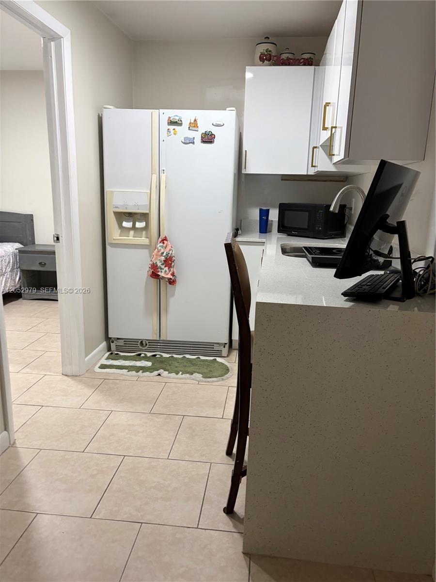 A small kitchen area features white cabinets, a refrigerator, and a countertop with a computer — MIAMI, FL