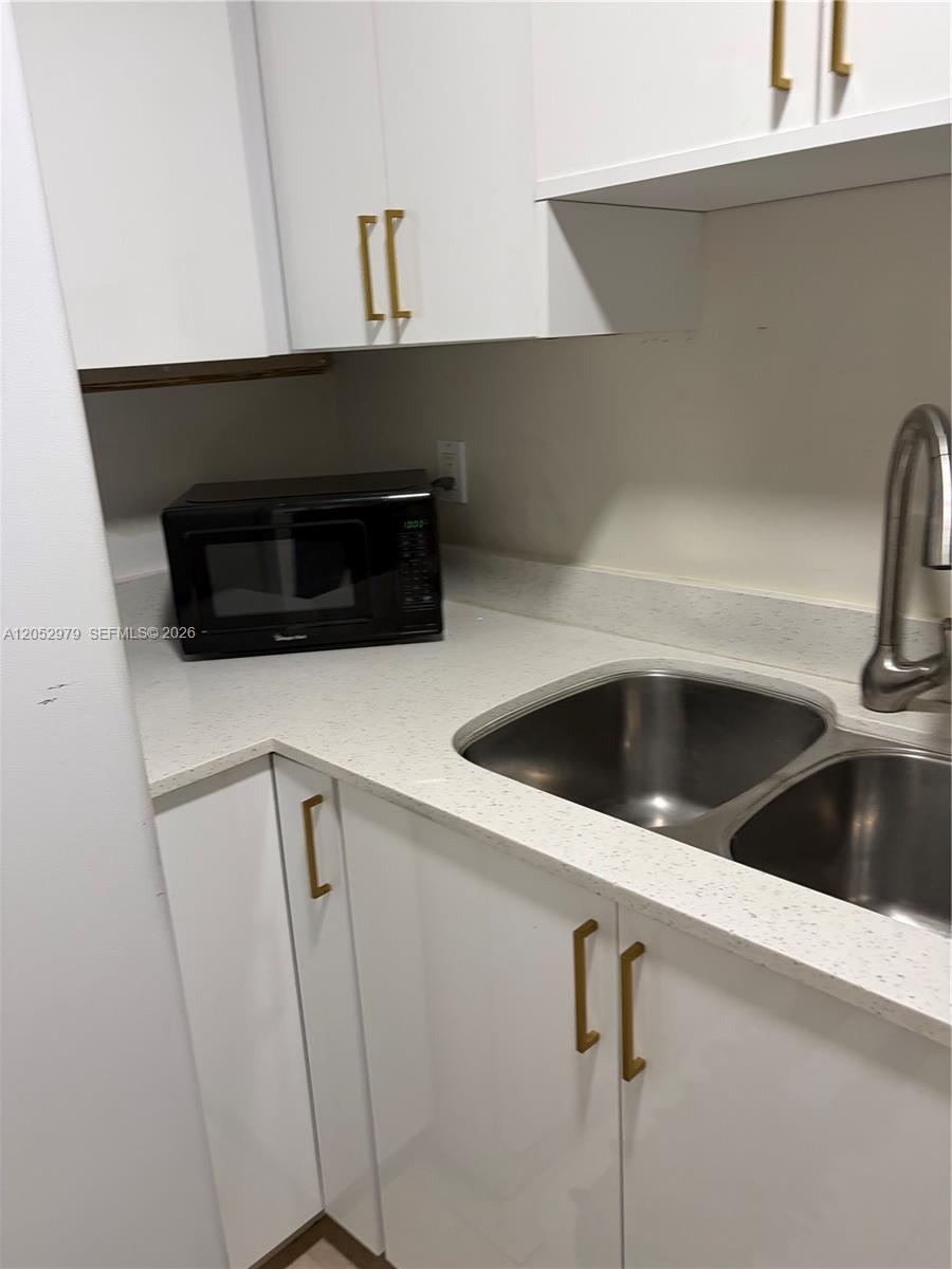 A kitchen features white cabinets, gold hardware, a double sink, and a black microwave — MIAMI, FL