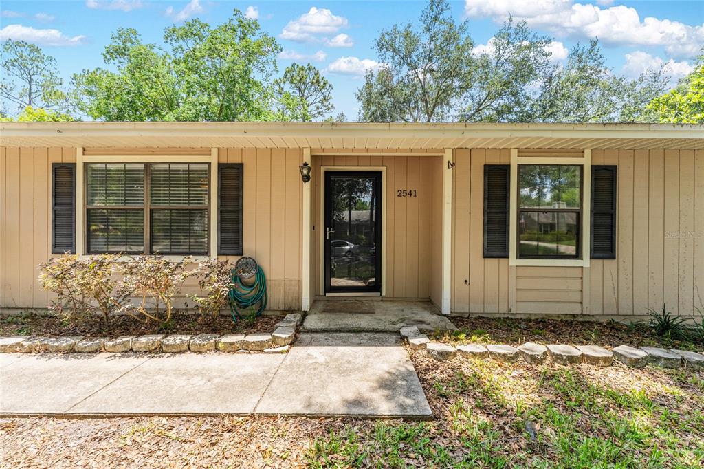 The exterior of a single-story house features tan siding, dark shutters, and a front entrance — 2541 NW 52ND PLACE, GAINESVILLE, FL