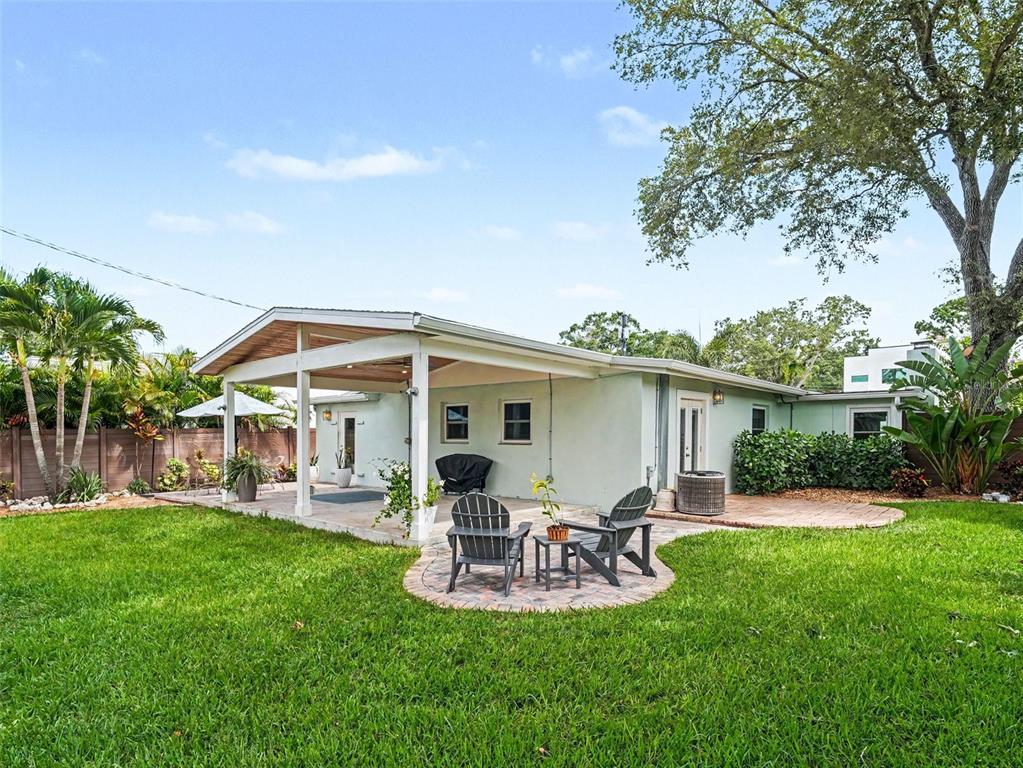 A backyard view of a light green house with a covered patio and brick pavers — 2344 TEMPLE STREET, SARASOTA, FL