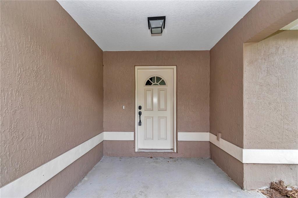A covered entryway features a beige front door with a window and tan stucco walls — 6781 NW 47TH AVENUE, OCALA, FL