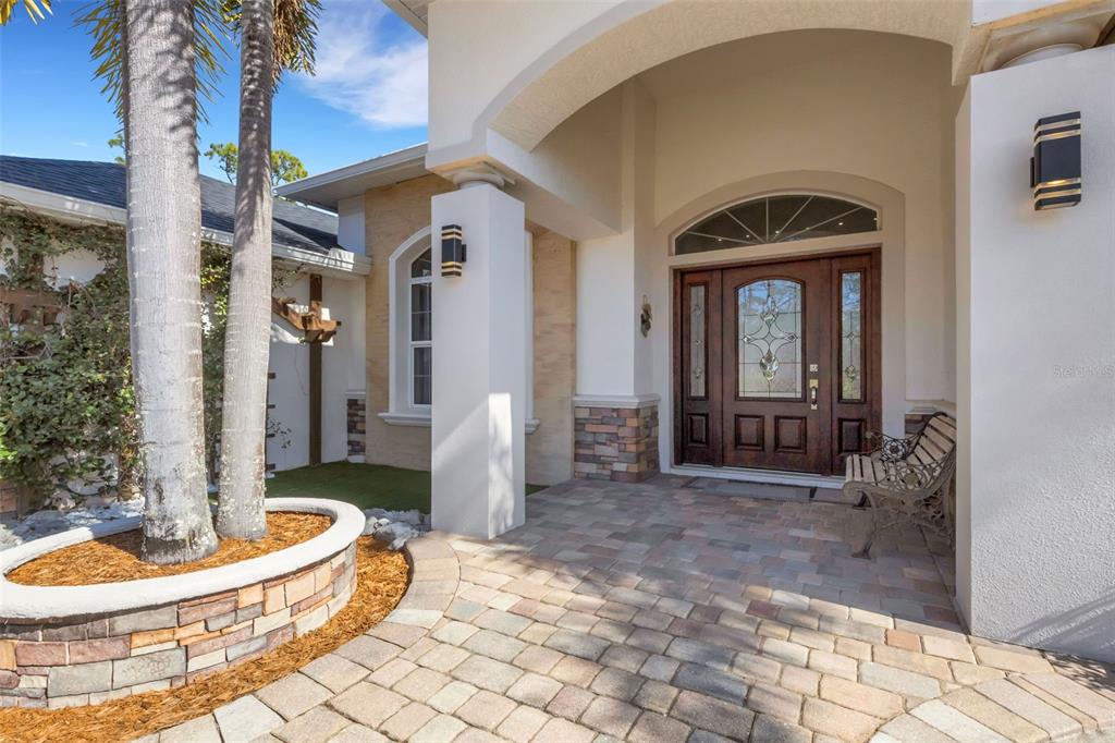 A paved entryway features a stone-accented planter, palm trees, and a decorative wooden front door — 13471 EISENHOWER DRIVE, PORT CHARLOTTE, FL