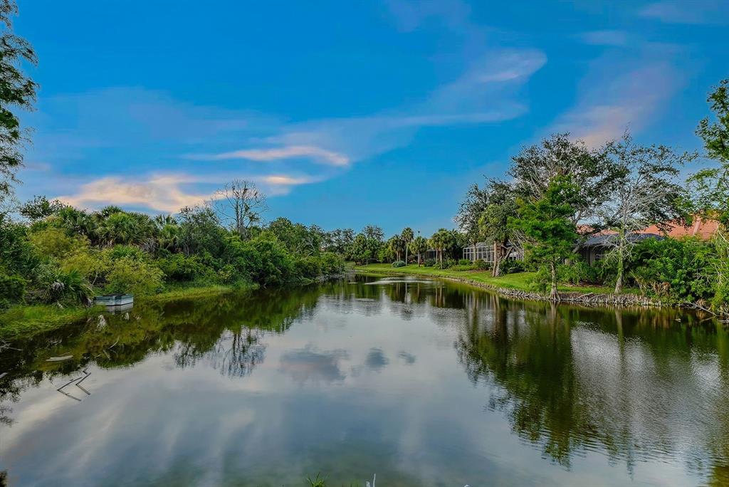 A calm pond reflects the blue sky and surrounding trees in a residential neighborhood — 24 GRAND PALMS BOULEVARD, ENGLEWOOD, FL