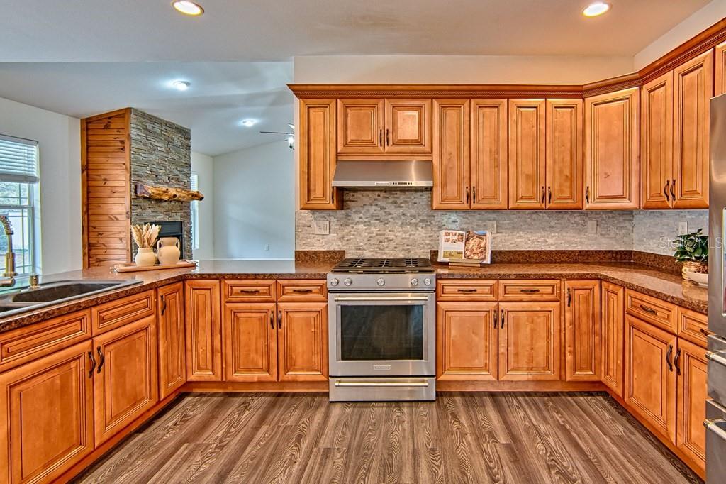 A kitchen with wood cabinets, stainless steel appliances, and a stone-accented fireplace in the background — 9880 NW 110TH STREET, CHIEFLAND, FL