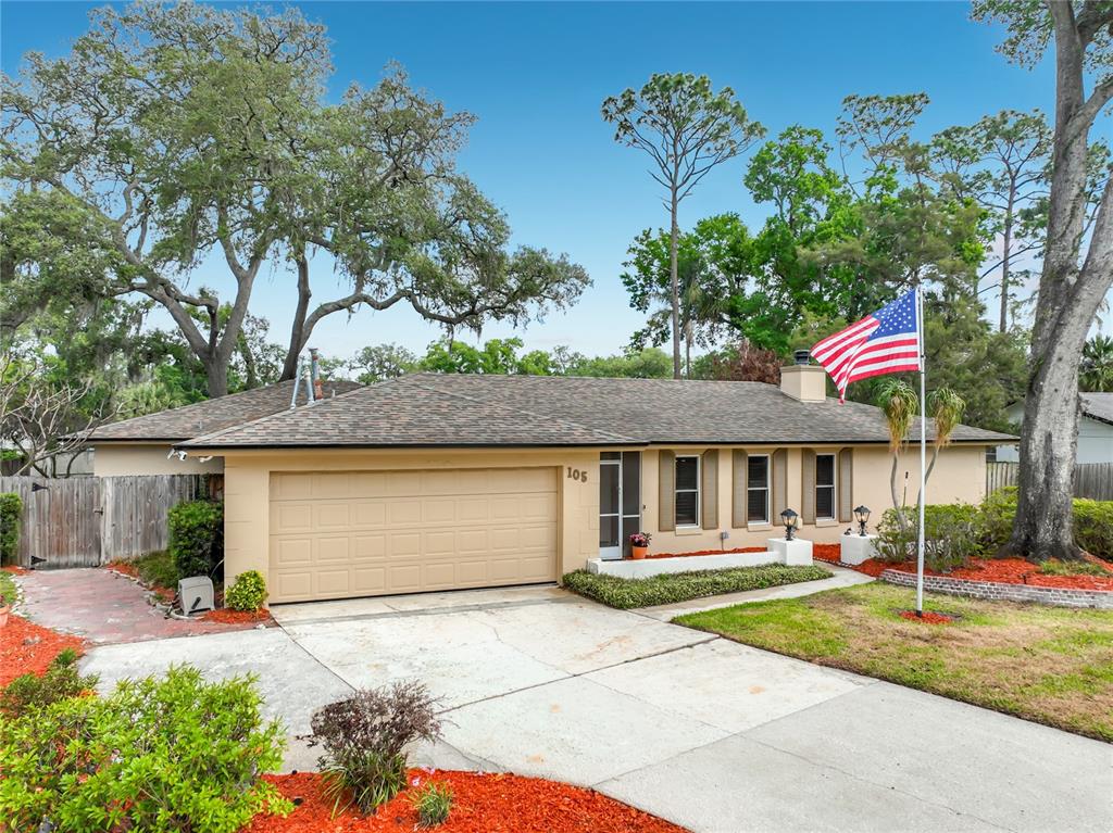 A single-story house with a beige exterior, a two-car garage, and an American flag — 105 CEDAR OAK TRAIL, LONGWOOD, FL