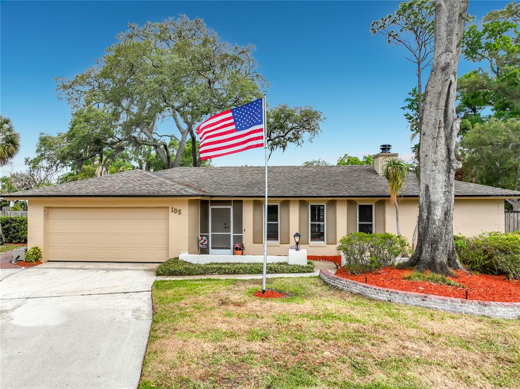 A single-story house with a tan exterior, a two-car garage, and an American flag — 105 CEDAR OAK TRAIL, LONGWOOD, FL