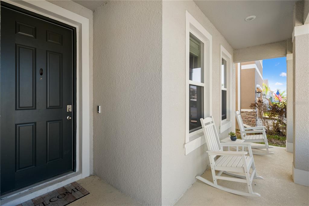 A covered front porch features a dark door, two white rocking chairs, and light-colored stucco — 6199 WANDERING WILLOW DRIVE, WESLEY CHAPEL, FL