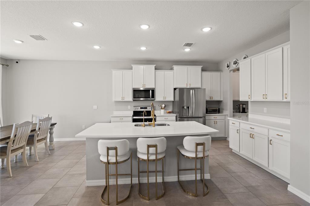 A modern kitchen features white cabinetry, a central island with bar stools, and stainless appliances — 6199 WANDERING WILLOW DRIVE, WESLEY CHAPEL, FL
