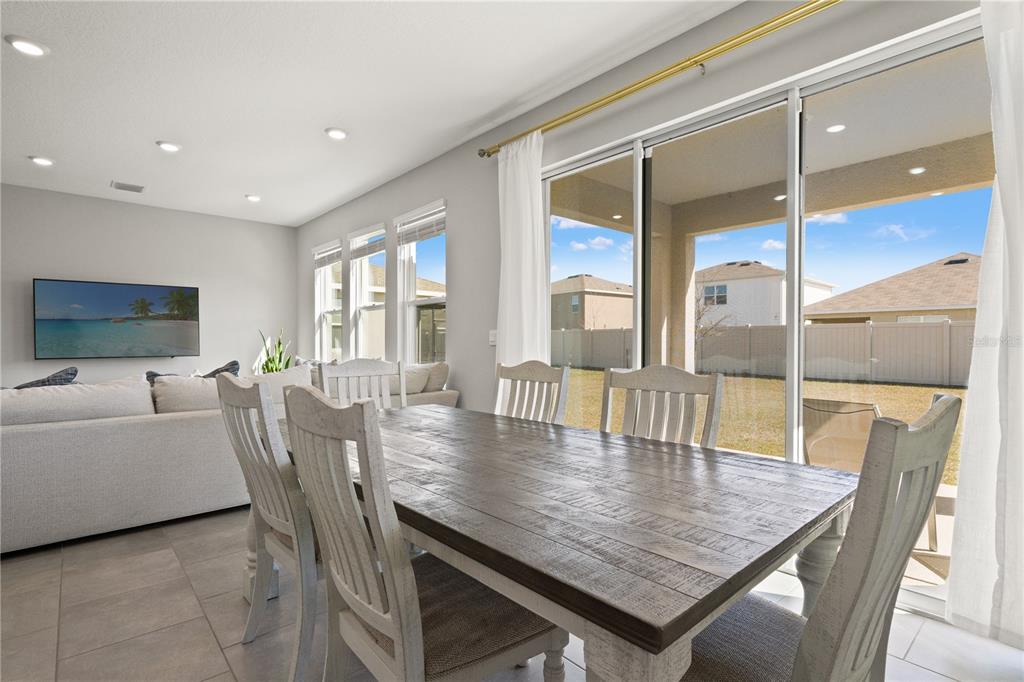 A dining area with a wooden table and chairs sits beside a large sliding glass door — 6199 WANDERING WILLOW DRIVE, WESLEY CHAPEL, FL