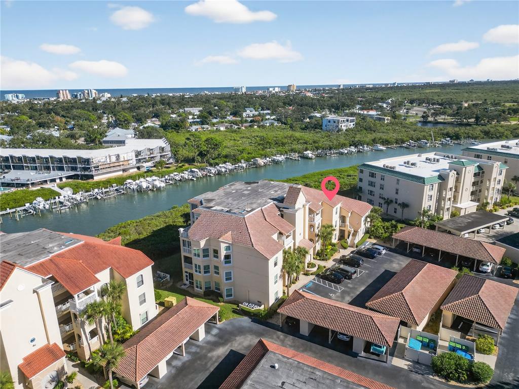 An aerial view shows a multi-story apartment complex with a parking lot and canal — 434 BOUCHELLE DRIVE UNIT 304, NEW SMYRNA BEACH, FL