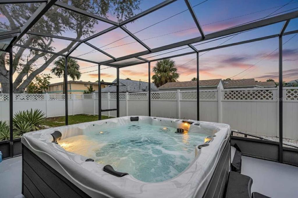 A hot tub sits on a patio enclosed by a screened-in lanai with a fenced yard — 3002 58TH STREET S, GULFPORT, FL