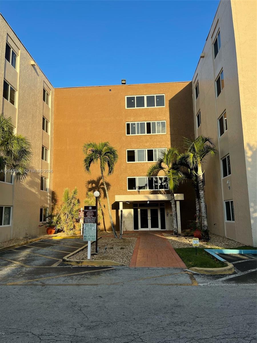 The exterior of a multi-story apartment building features a central entrance with palm trees — 6950 Miami Gardens Dr # 312A, Hialeah FL 33015, HIALEAH, FL