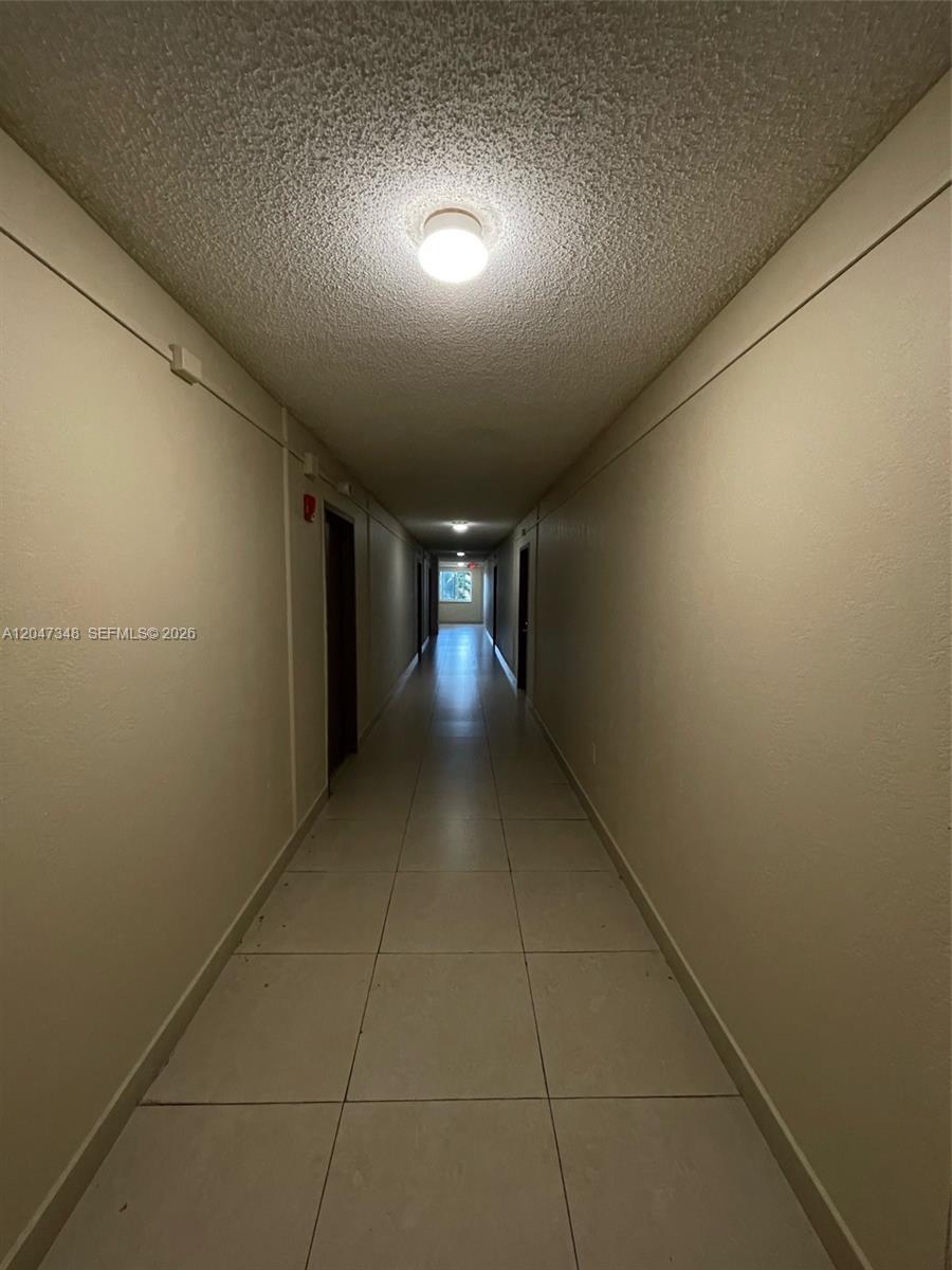 A long, narrow indoor hallway features beige walls, a tiled floor, and a popcorn ceiling — 6950 Miami Gardens Dr # 312A, Hialeah FL 33015, HIALEAH, FL
