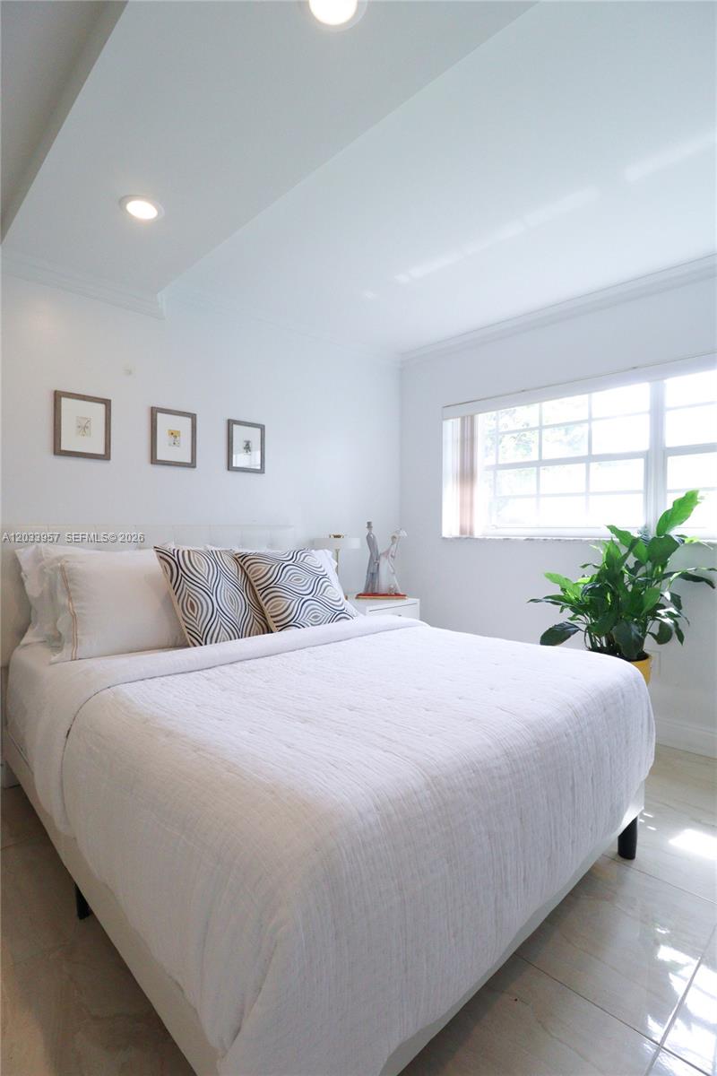 A bedroom features a white bed, a potted plant, and three framed pictures on the wall — 7797 Golf Circle Drive # 208J, Margate FL 33063, MARGATE, FL