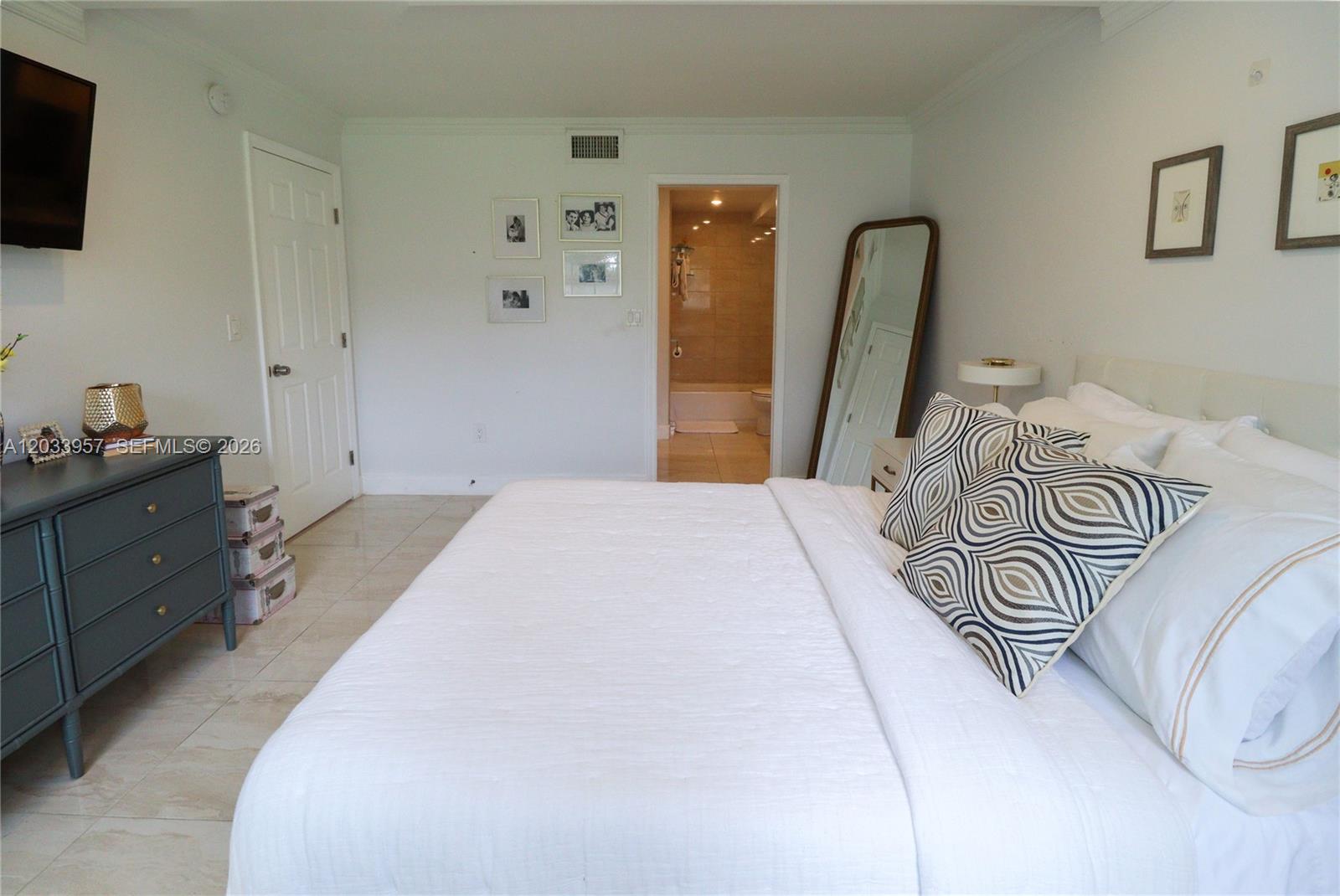 A bedroom features a white bed, a grey dresser, and an open doorway to a bathroom — 7797 Golf Circle Drive # 208J, Margate FL 33063, MARGATE, FL