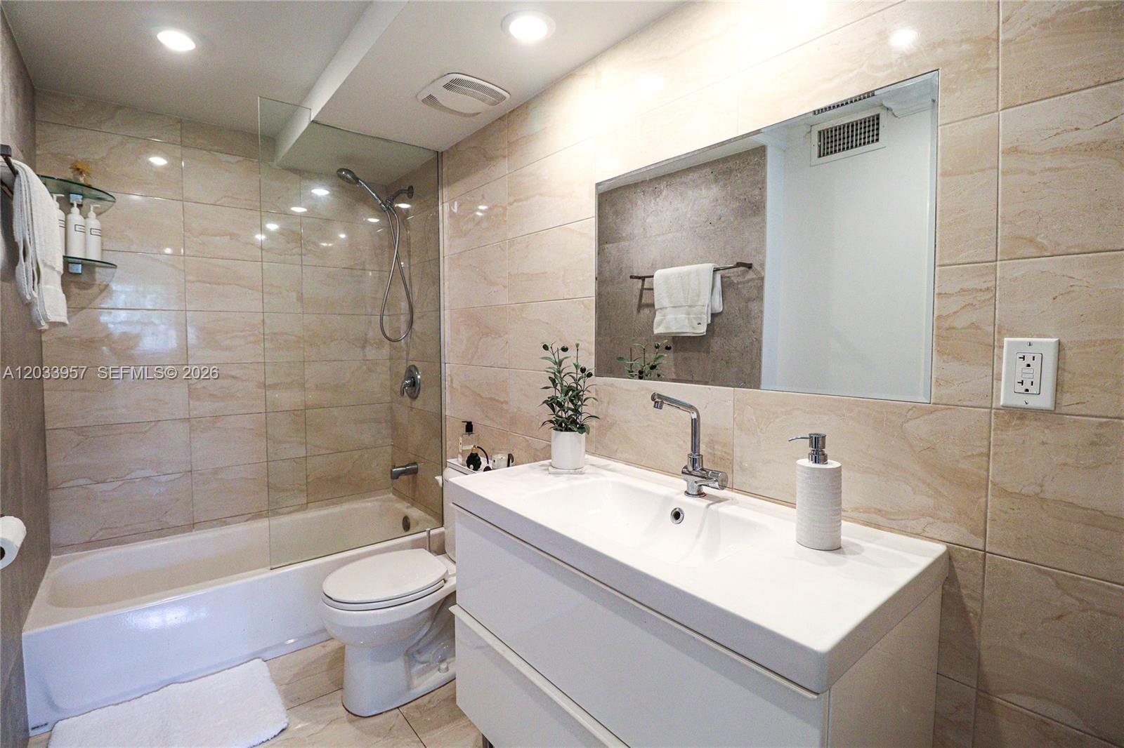 A modern bathroom features a white vanity, a glass-enclosed shower, and beige tiled walls — 7797 Golf Circle Drive # 208J, Margate FL 33063, MARGATE, FL