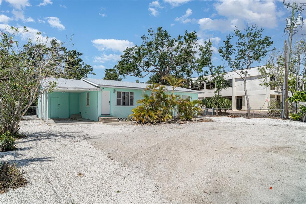 A light green single-story house with a gravel driveway and a carport under a blue sky — 5026 CALLE MINORGA, SARASOTA, FL