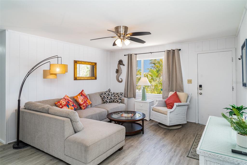 A living room features a sectional sofa, a wicker armchair, and white paneled walls — 5026 CALLE MINORGA, SARASOTA, FL