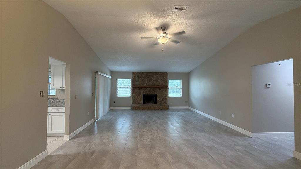 A spacious living room features light tile flooring, a stone fireplace, and a ceiling fan — 6434 ROCKINGTREE LANE, ORLANDO, FL